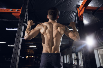 Fototapeta na wymiar Young healthy man, athlete doing exercises, pull-ups in gym. Single caucasian model practicing hard, training his upper body. Concept of healthy lifestyle, sport, fitness, bodybuilding, wellbeing.