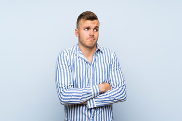 Young handsome blonde man over isolated blue background making doubts gesture while lifting the...