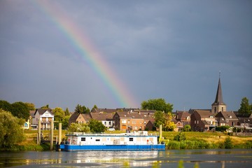 house boat on river with rainbow in european town