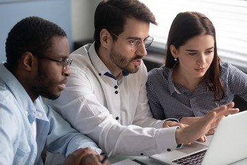 Three diverse colleagues looking at laptop screen working together indoors