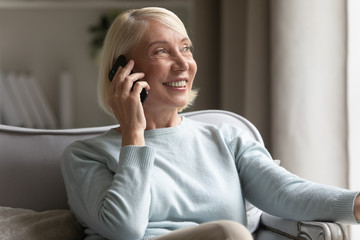 Smiling mature woman look in distance talking on cell