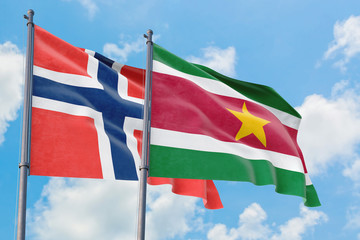 Suriname and Bouvet Islands flags waving in the wind against white cloudy blue sky together. Diplomacy concept, international relations.