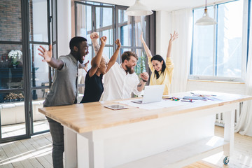 Excited multiethnic coworkers celebrating success while using laptop at office