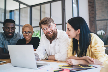 Cheerful confident diverse people using laptop while having discussion