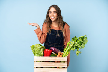 Farmer with freshly picked vegetables in a box holding copyspace imaginary on the palm to insert an ad