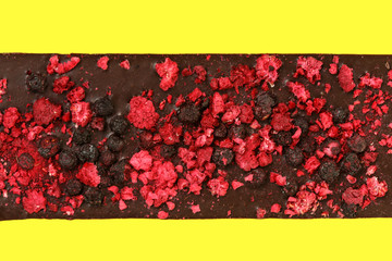 Bar of black chocolate with pieces of red raspberries isolated on yellow
