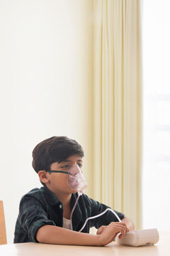 Young boy sitting and inhaling through a nebuliser at home. (Children) 