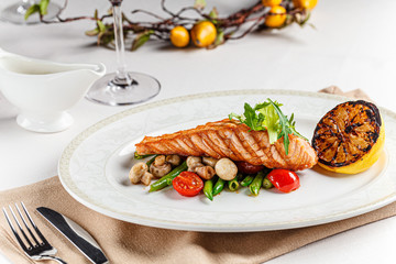 European cuisine. A large steak of red salmon fish, with mushrooms, asparagus, cherry tomatoes and fried lemon. Serving dishes in a restaurant on a white plate.