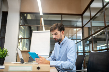 Bearded man in a blue shirt holding a tablet