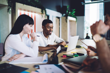 Captivated multiracial colleagues discussing project and surfing laptop during meeting