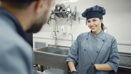 Two chefs in gray uniform are talking to each other while cooking in commercial kitchen, picture...