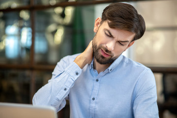 Obraz premium Bearded man in a blue shirt having pain in his neck