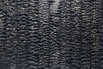 Charred boards in a vertical position. The inner wall of a wooden building after a fire. Texture of burnt wood.