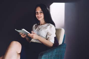 Beautiful pleased woman with gadget chilling in chair