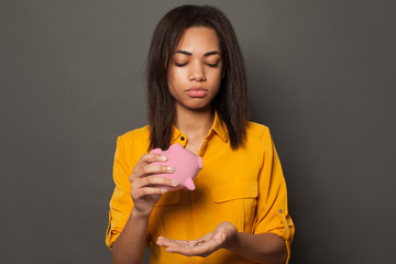 Sad poor woman holding piggy bank without money