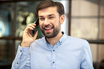 Young bearded man in a blue shirt talking on the phone and feeling awesome