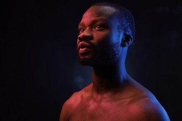 portrait of a handsome black man in red and blue light on dark background  with naked sports torso - 320550900