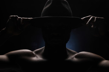 no face portrait of a black man in dark hat with naked sports torso on dark background