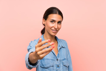 Young woman over isolated pink background inviting to come