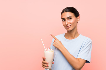 Young woman with strawberry milkshake over isolated pink background pointing to the side to present a product