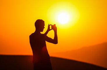 Silhouette of a man photographing a sunset on the phone on the background of a golden sun