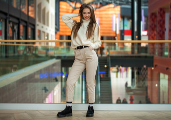 Portrait of a young beautiful woman in beige sweater and pants posing in the mall