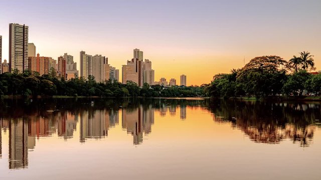 View of a city lake on a beautiful sunset. Lake shore with a green area of trees, and few buildings of the city on background. Video of Igapo lake at Londrina PR Brazil.