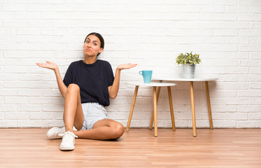 Young woman sitting on the floor having doubts with confuse face expression