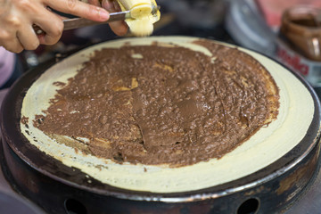 Thai pancakes preparation: the cook cuts a banana into slices directly on a fried pancake with chocolate paste. street food close up