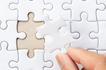 Closed up background of white plain jigsaw with hand that hold missing piece to match or fulfill