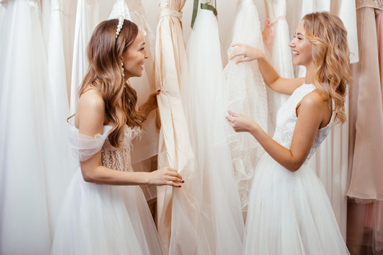 young caucasian friends choosing, trying on wedding dresses in salon, beautiful women preparing for wedding, to celebrate, dream to be bride