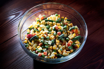 Frozen different vegetables in a glass plate on a wooden background.