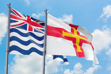 Guernsey and British Indian Ocean Territory flags waving in the wind against white cloudy blue sky together. Diplomacy concept, international relations.