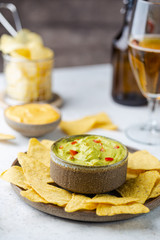 Nachos chips in a bowl with sauces guacamole and beer over white stone background.