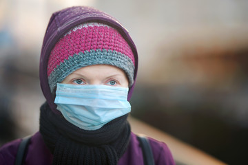 Portrait of young woman on city street in medical face mask as protection from spreading virus, flu diseases, influenza in public spaces. Female wearing surgical mask while walking on city street
