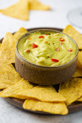 Nachos chips in a bowl with sauces guacamole and beer over white stone background.