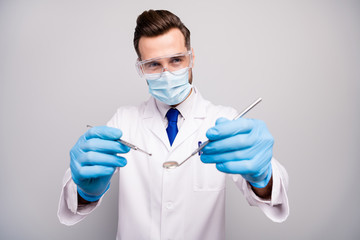 Close-up portrait of his he nice attractive experienced qualified doc dentist holding in hands steel instrument preparing surgery isolated on light white gray pastel color background
