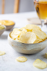 Crunchy delicious potato chips in a bowl with beer for a tasty snack break on light background