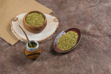 Yerba mate with bombilla in calabash and in wooden bowl and on ceramic stand on stone bakground