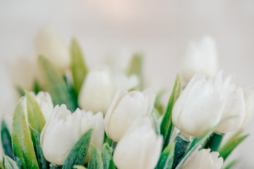 Obraz na płótnie Canvas Beautiful white tulips. White spring flowers in greenery. Artificial Indoor Tulips. Bouquet of white tulips with a place for an inscription.