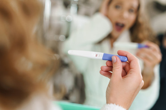 Image of young woman holding pregnancy test after shower in bathroom