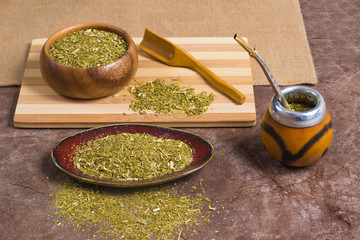 Yerba mate in calabash and in bowls with scoop on stone background