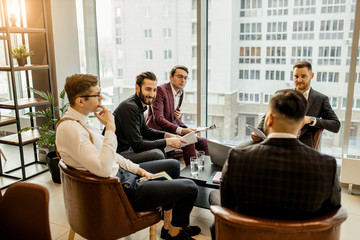 Obraz na płótnie Canvas coworking of business team consisted of young successful men wearing formal suits, developing business projects together and discussing business partnership, interaction of diverse business people