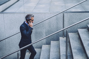 Serious mature businessman calling by smartphone on stairs