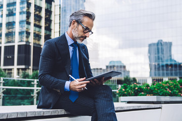 Mature businessman holding tablet with stylus inn modern city