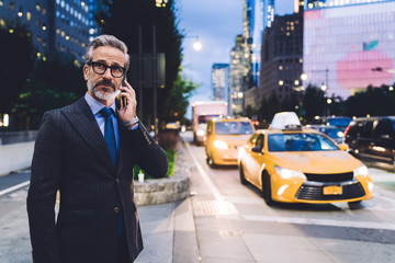 Adult businessman talking on smartphone against evening New York road