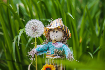 Toy scarecrow with a dandelion in a flower garden,