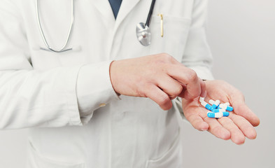 Cropped image of unrecognizable doctor having handful of blue and white gelatin capsules trying to take one