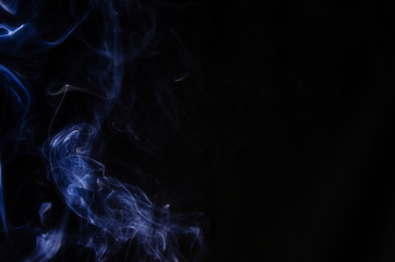 Abstract figure made of blue smoke on the left side of the frame on a dark background with place for text.