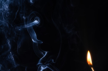 Fototapeta premium Fire with an abstract figure from blue smoke on a dark background with a place for text, fantasy,fiction, mysticism, magic.
